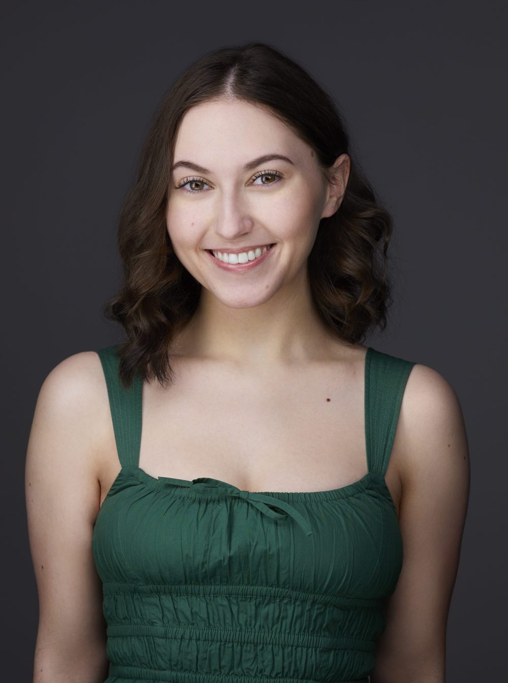 Smiling woman in a green dress against a dark background.