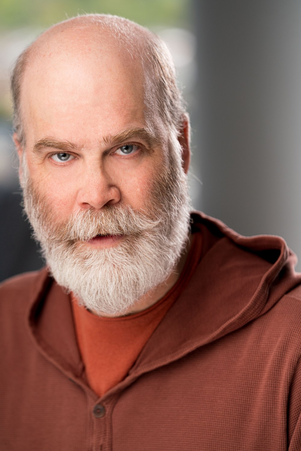 Bald man with white beard and brown hoodie looking directly at the camera.